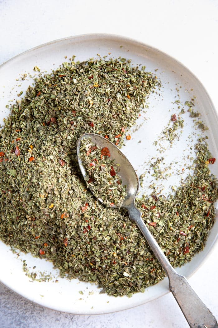 Mixed together dried herbs for on a white plate for Italian seasoning.