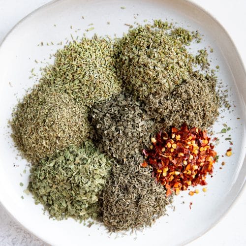 Piles of different dried herbs on a white serving plate.