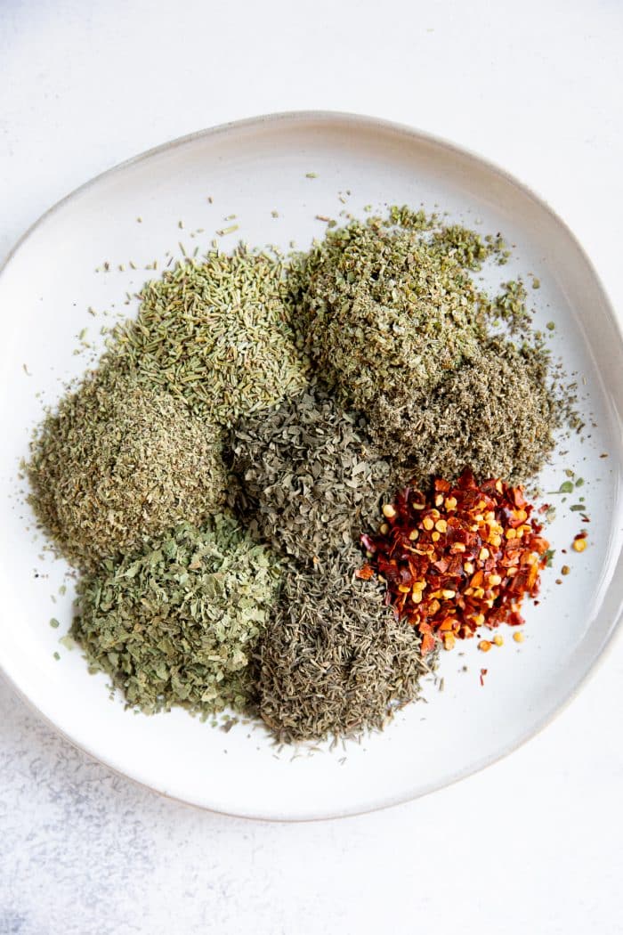 Piles of different dried herbs on a white serving plate.