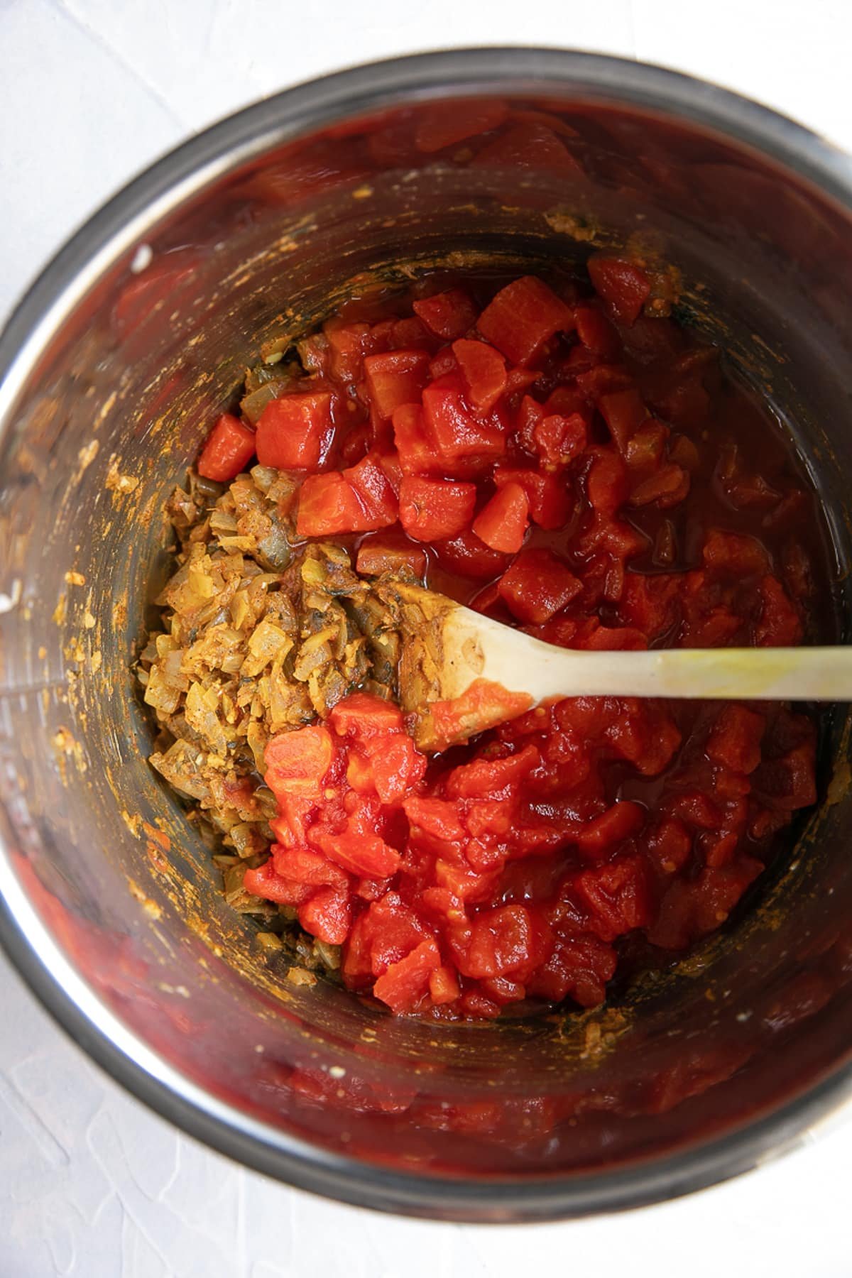 Onions and spices sauteeing in the bowl of an Instant pot with canned tomatoes.