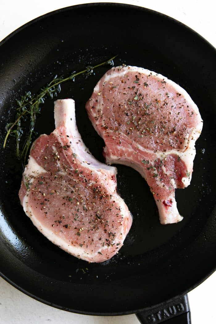 Duas costeletas de porco com osso cozinhadas numa frigideira de ferro fundido médio.