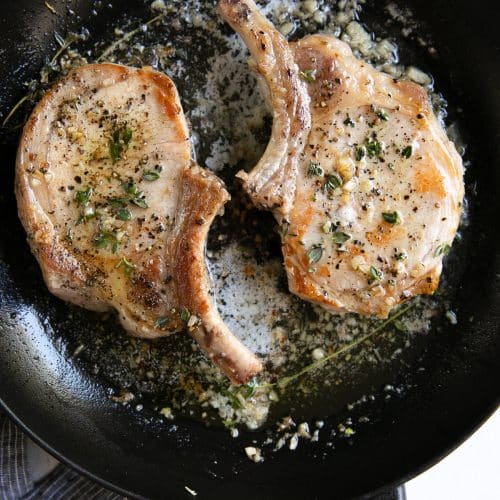 Two cooked bone-in garlic butter and thyme pork chops.