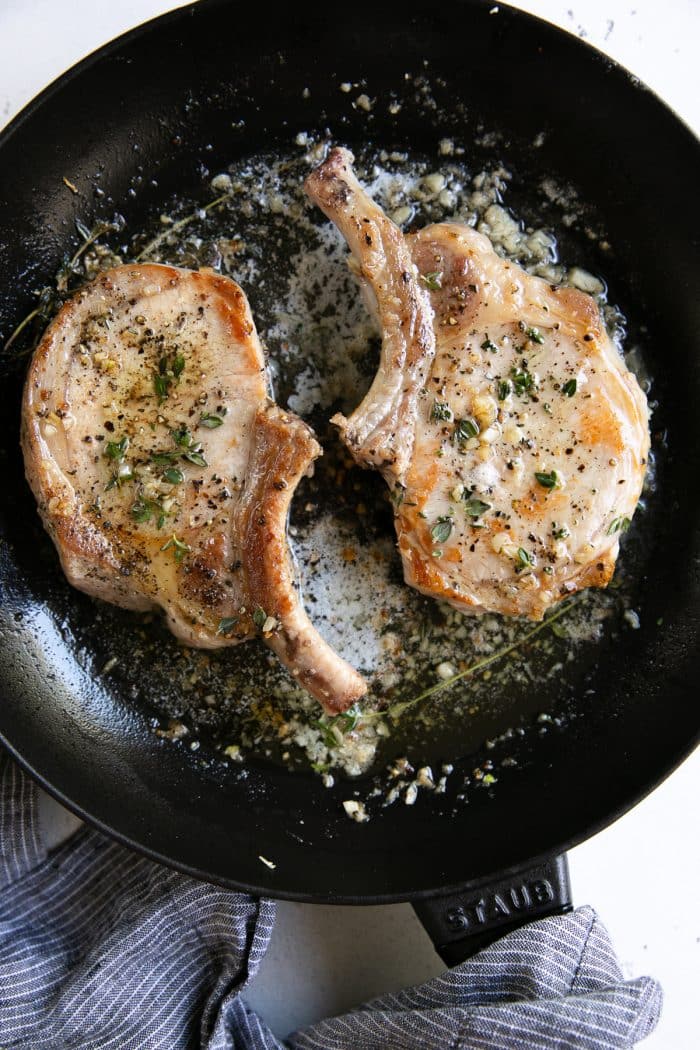 Two cooked bone-in garlic butter and thyme pork chops.