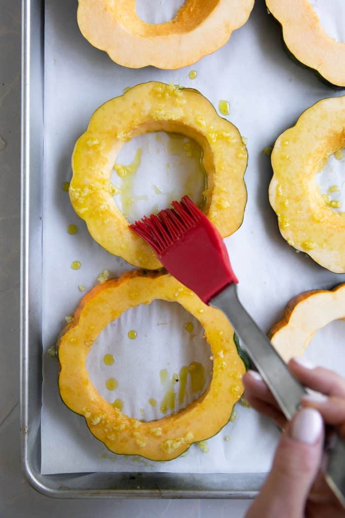 Brushing acorn squash rings with olive oil.