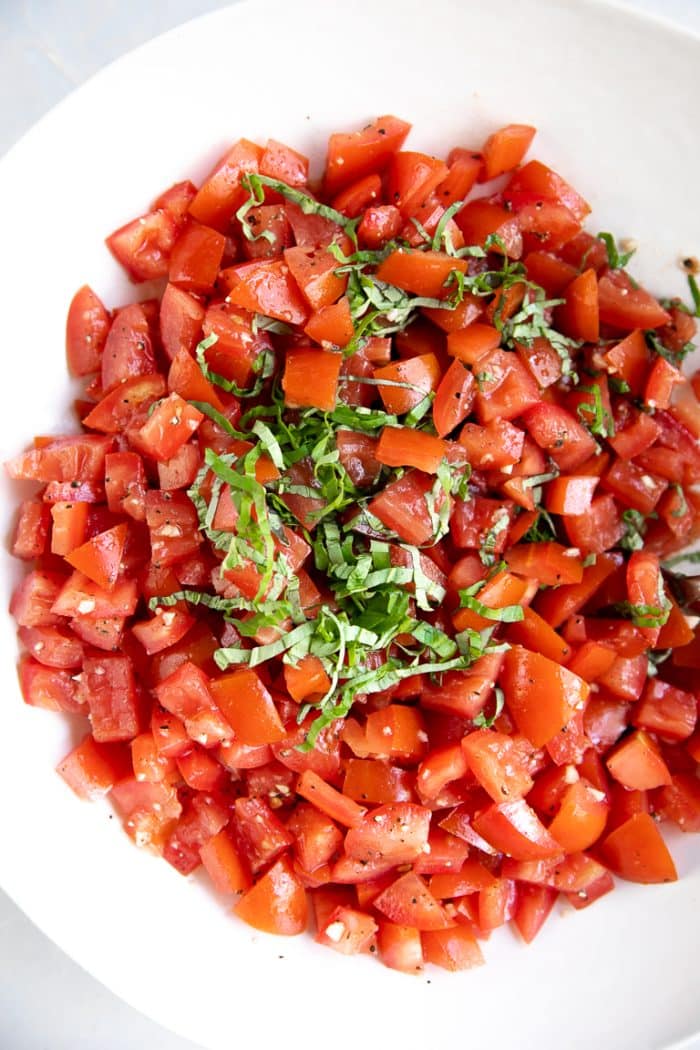 Large white bowl filled with diced tomatoes, minced garlic, and fresh basil.