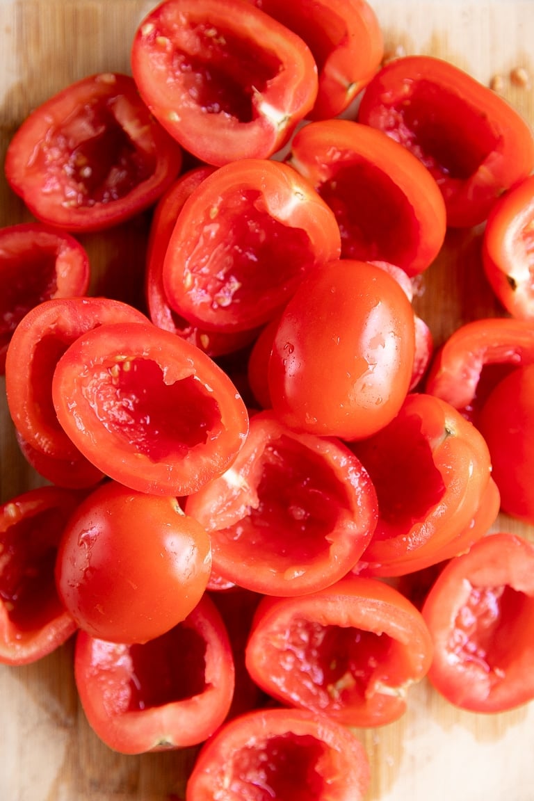 Pile of halved and seeded Roma tomatoes on a large cutting board.