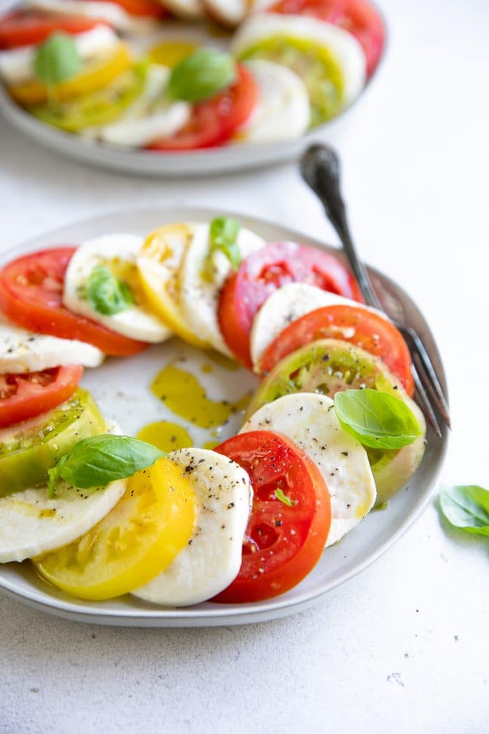 Fresh sliced mozzarella cheese and tomatoes on a small salad plate garnished with fresh basil, olive oil, salt, and pepper.