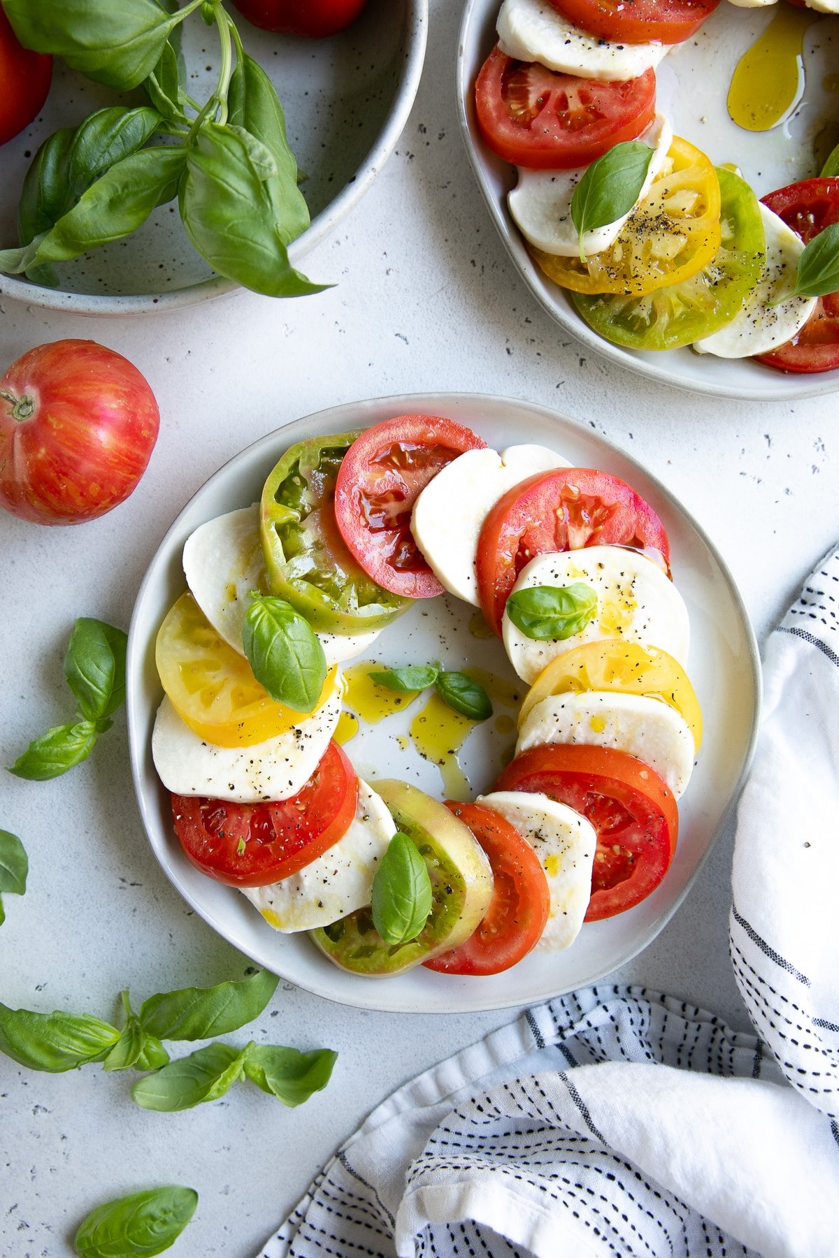 Plate filled with overlapping slices of fresh tomatoes and mozzarella cheese drizzled with olive oil and garnished with fresh basil.