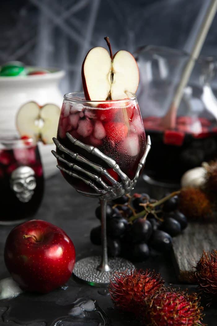 Large skeleton hand wine goblet filled with red sangria made with raspberries, blackberries, apples, and Sprite.