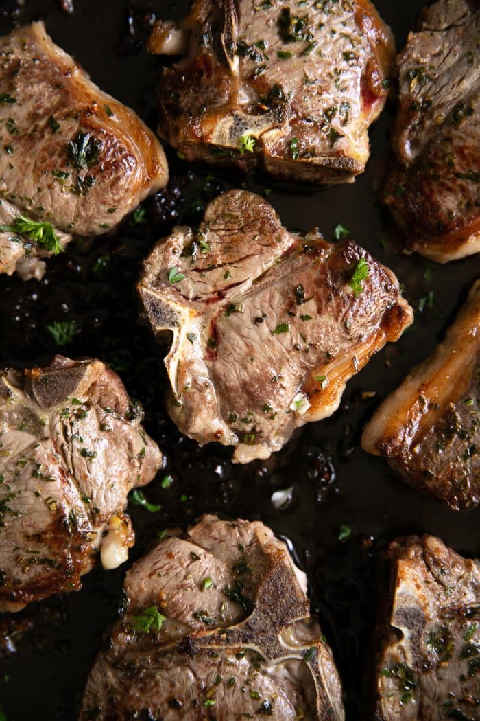 Large skillet filled with completely cooked garlic herb lamb chops.