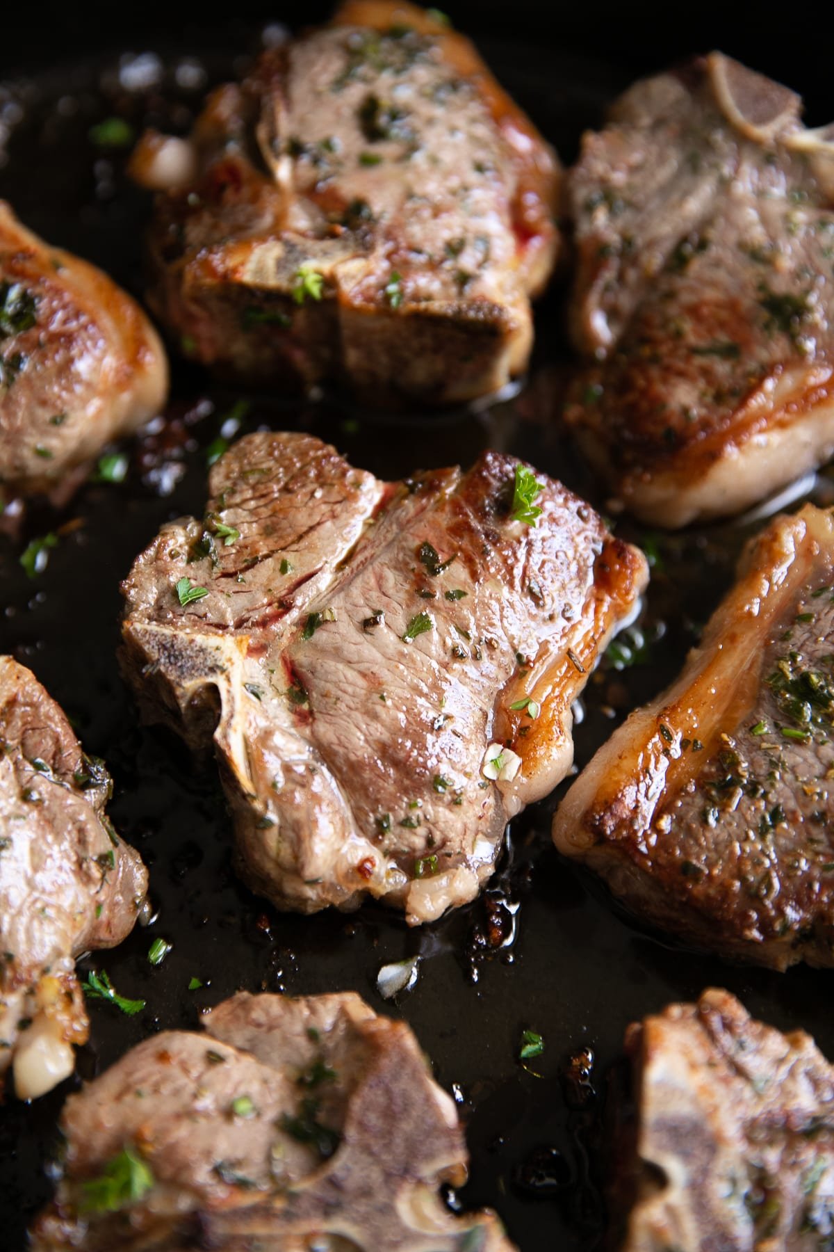 Six Garlic and herb marinated lamb chops cooking in a large cast-iron skillet.