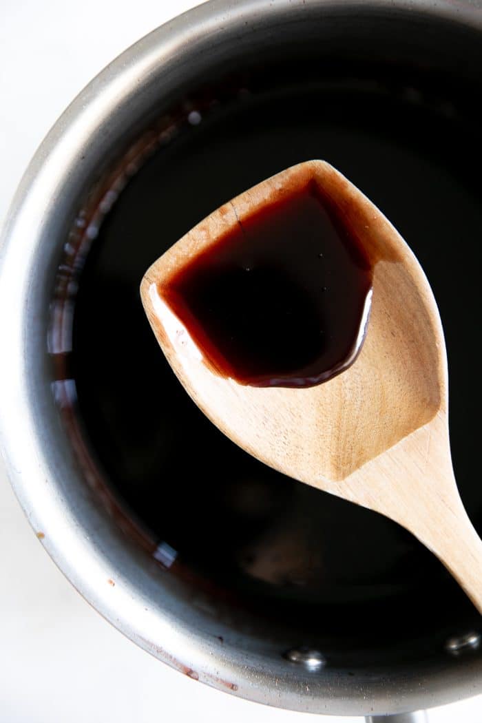 Wooden spoon balanced over a medium saucepan filled with homemade pomegranate molasses.