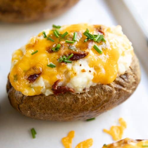 Twice baked potato on a baking sheet topped with cheese, bacon, and fresh chives.