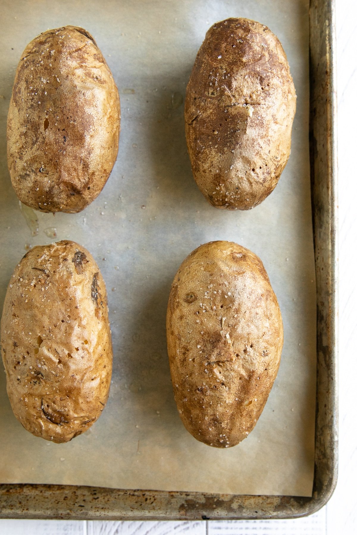 Four baked russet potatoes on a baking sheet fully cooked.