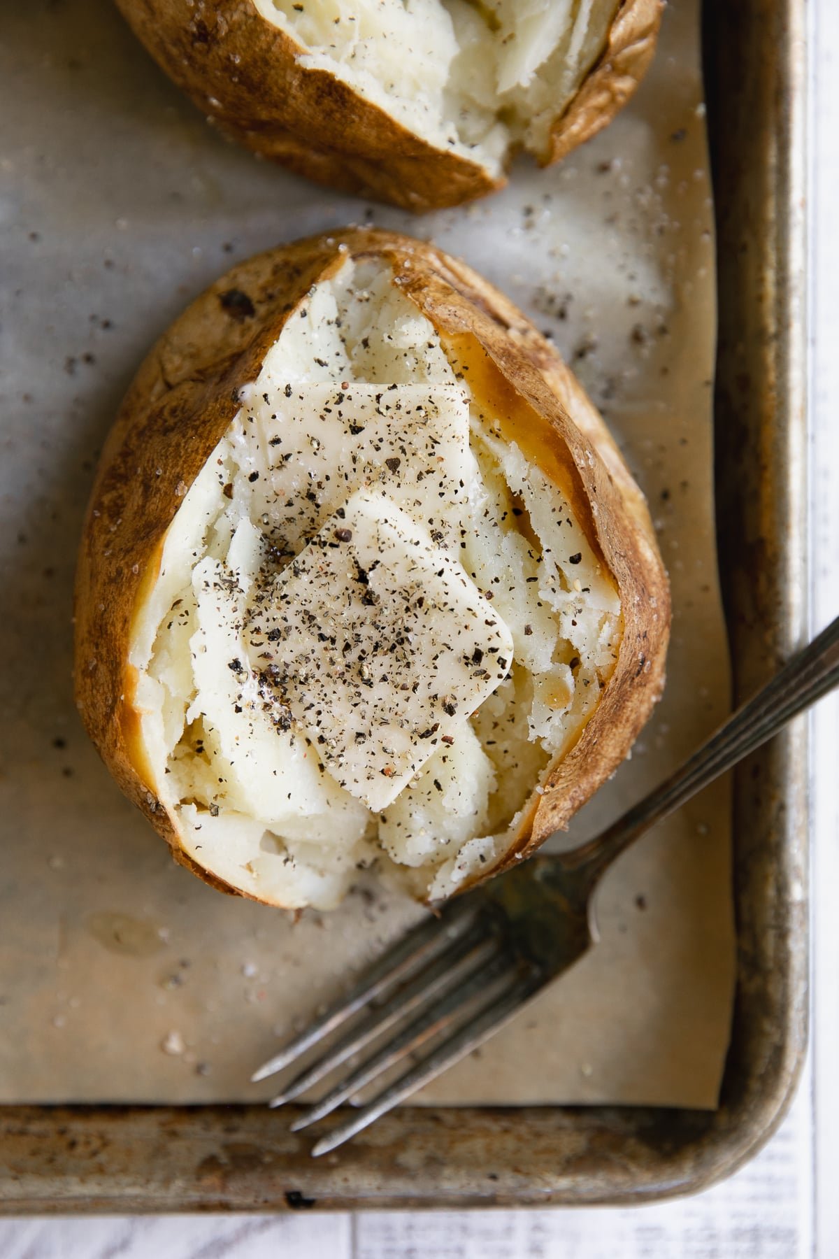 Overhead image of fully cooked baked potato topped with butter and seasoned with salt and pepper.