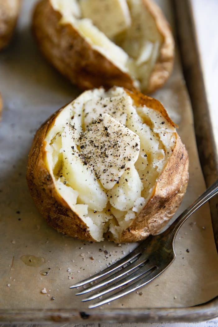 Fully cooked baked potatoes cut in half and seasoned with salt, pepper, and butter.