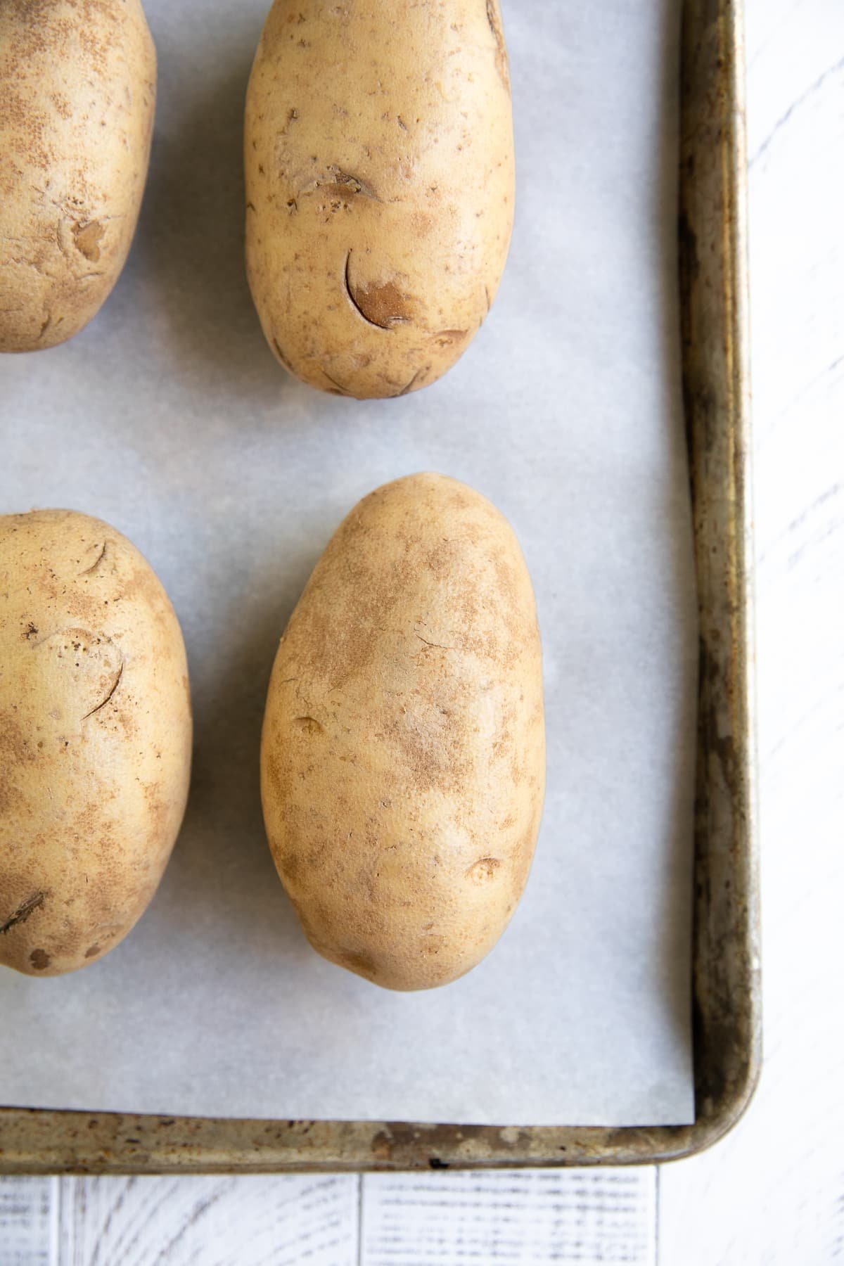 Unbaked washed russet potatoes on a baking sheet.