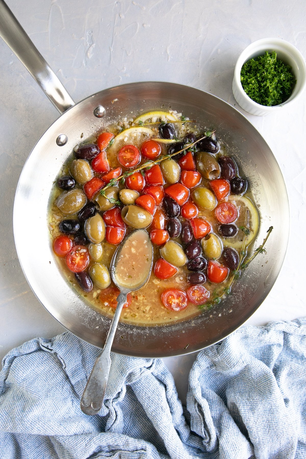 Skillet filled with a lemon, garlic, and white wine sauce with cherry tomatoes and olives.