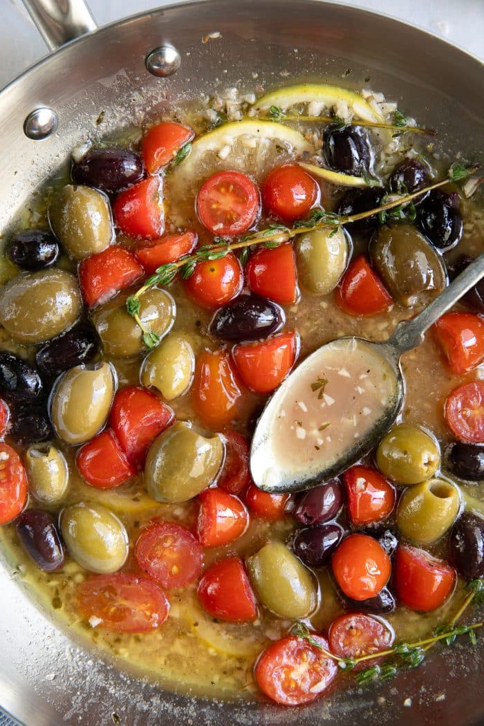 Skillet filled with a lemon, garlic, and white wine sauce with cherry tomatoes and olives.