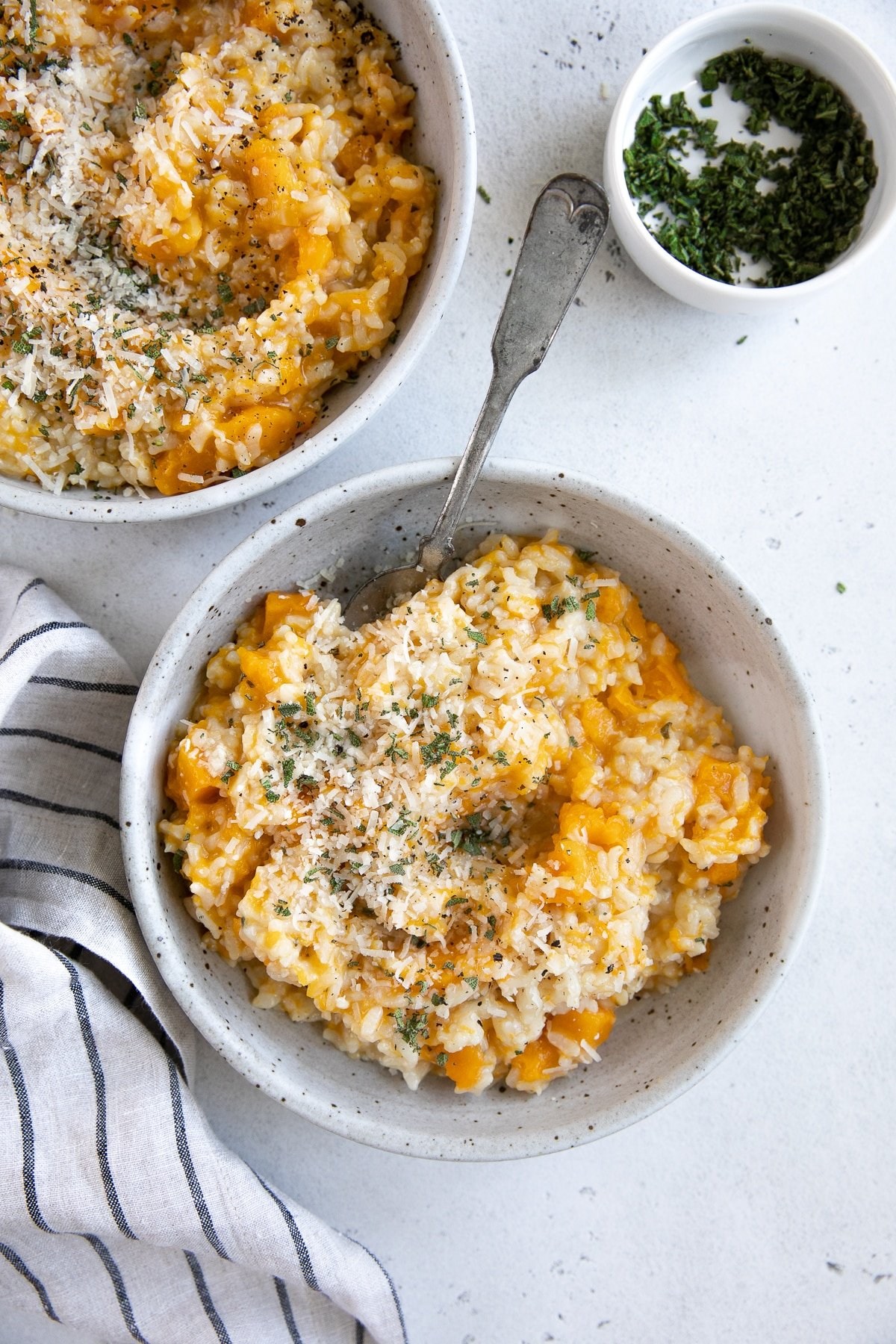 Two shallow ceramic bowls filled with creamy butternut squash risotto garnished with parmesan cheese and fresh sage.