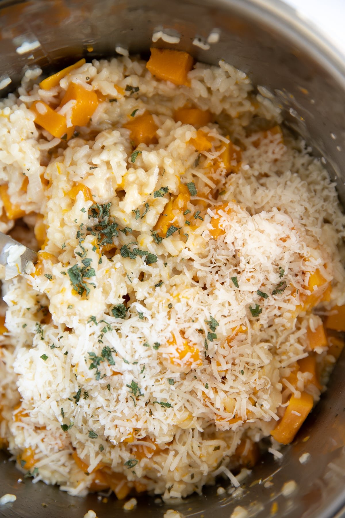 Instant Pot filled with cooked risotto and butternut squash garnished with parmesan cheese and minced sage.