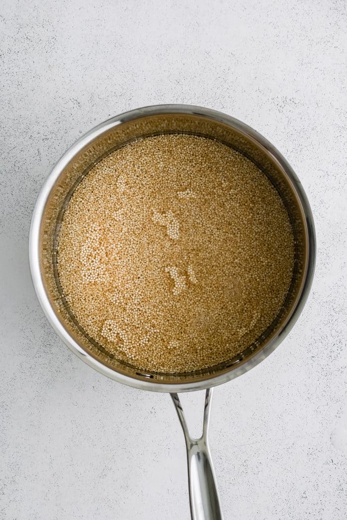 Large sauce pot filled with uncooked quinoa covered by water.