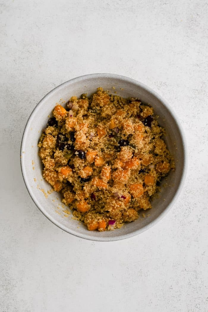 Mixing bowl filled with roasted cubes of butternut squash, diced red onion, dried cranberries, pumpkin seeds, and cooked quinoa all gently tossed together.