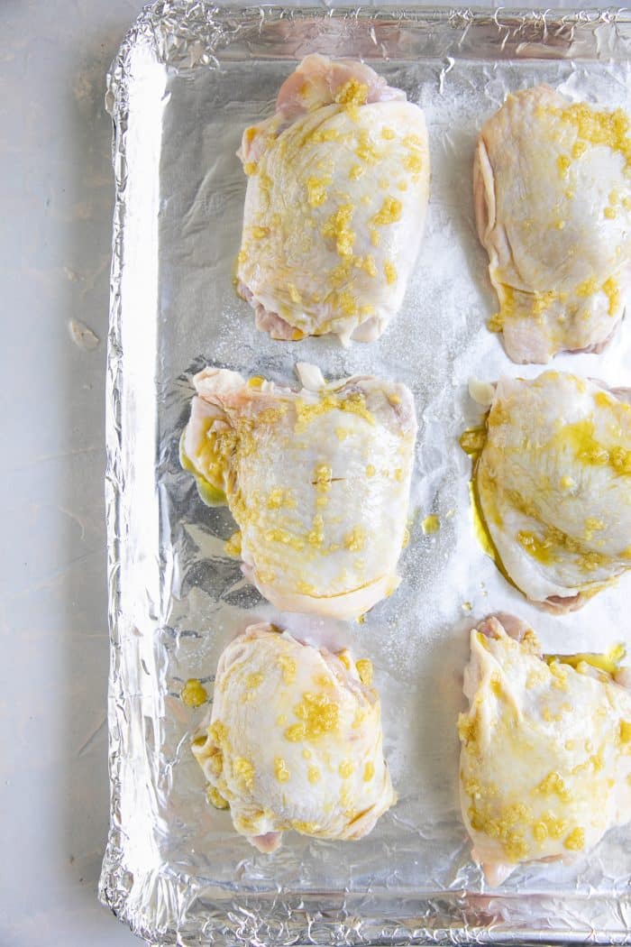 Six bone-in skin-on chicken thighs drizzled with olive oil and smothered with minced garlic.