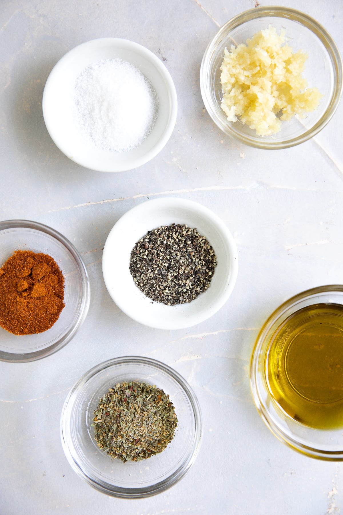 Small bowls filled with minced garlic, salt, pepper, paprika, Italian seasoning, and olive oil.