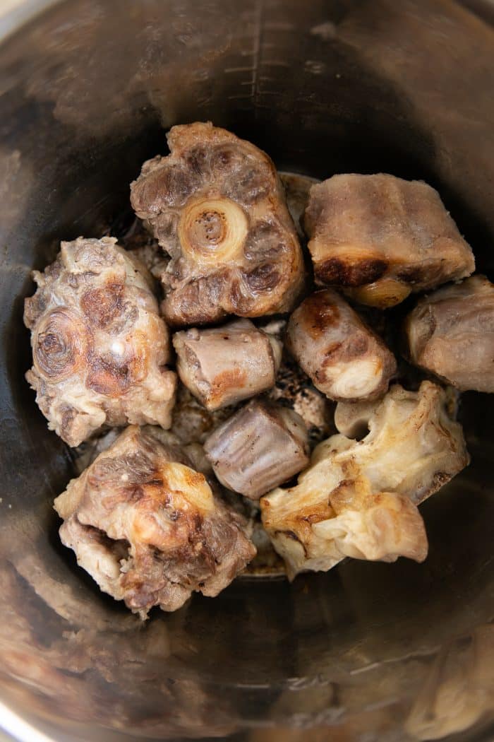 Beef bones browning in the bowl of a large Instant Pot.