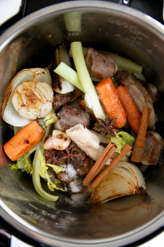 Instant Pot filled with beef bones, chicken feet, garlic, and charred vegetables.