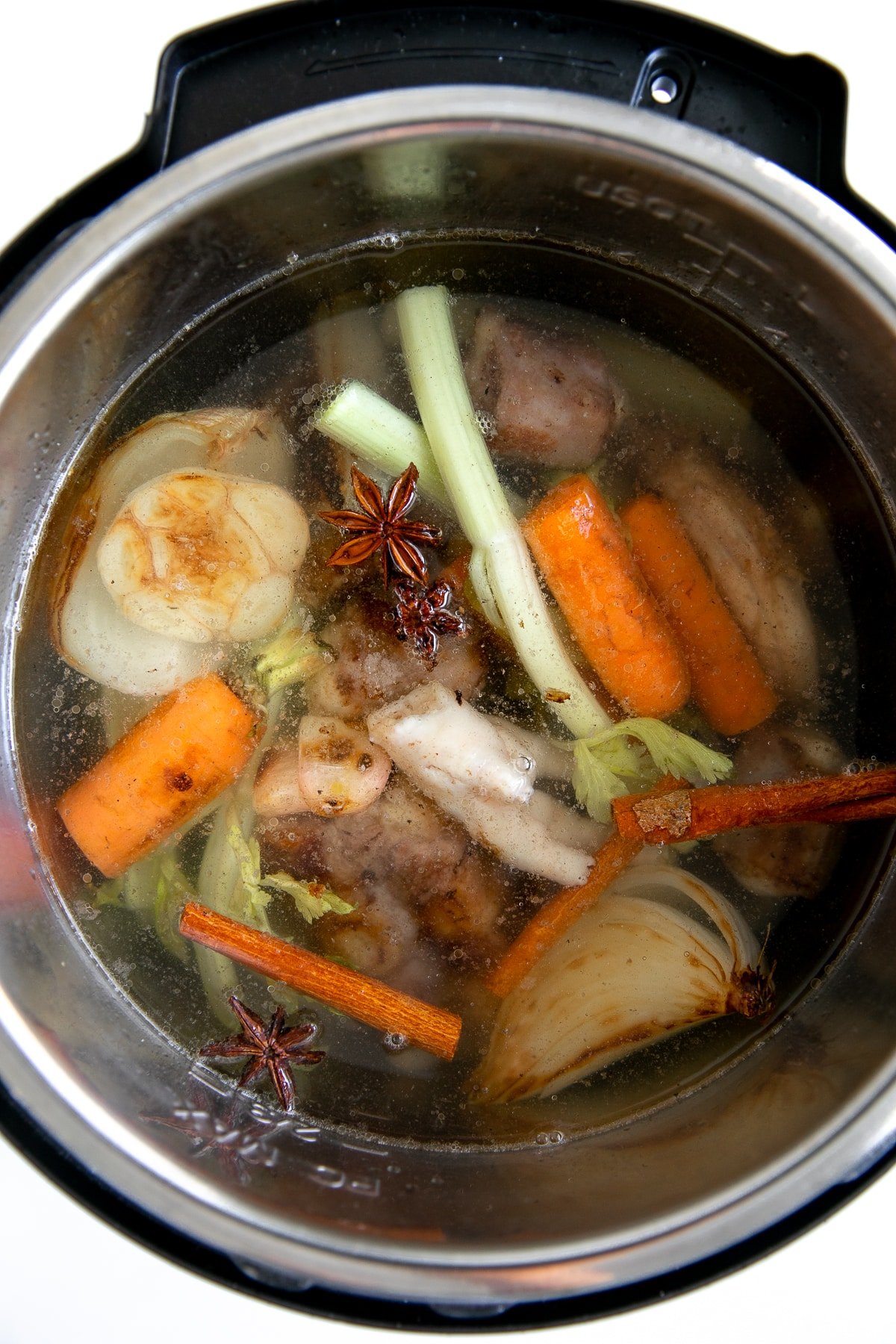 Instant Pot filled with beef bones, chicken feet, garlic, charred vegetables, star anise, cinnamon sticks, and filled three-fourths of the way full with water.