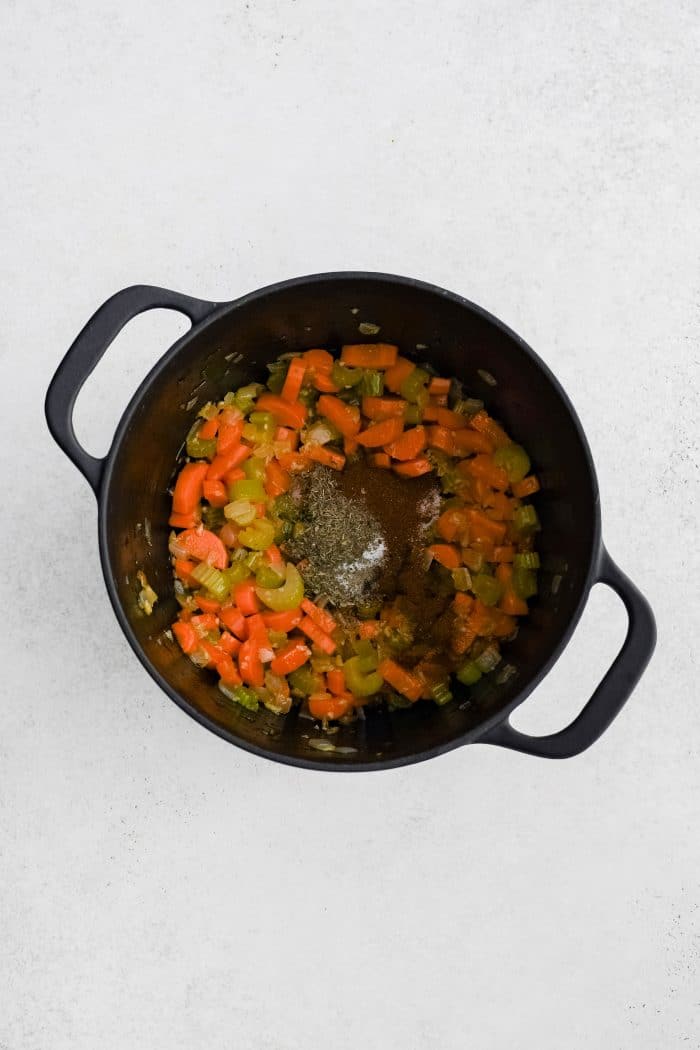 Paprika, dried thyme, dried basil, salt, and black pepper added to garlic, softened onion, carrots, and celery cooking in a large cast iron pot.