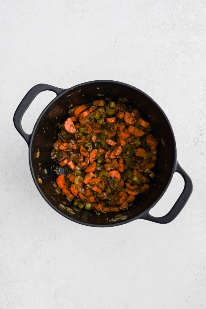 Softened onion, celery, and carrots combined with garlic, paprika, dried thyme, dried basil, salt, and black pepper in a large cast iron pot.