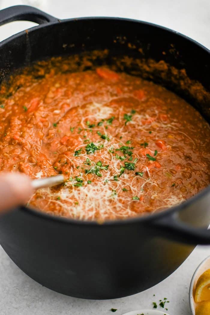 Ladle in a large pot of homemade lentil soup garnished with grated parmesan and fresh chopped parsley.