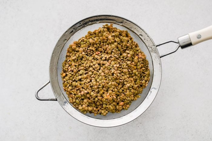 Brown lentils draining in a fine mesh strained resting on top of a bowl.