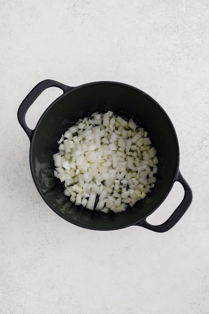 Diced onion cooking in butter and olive oil in a large cast iron pot.