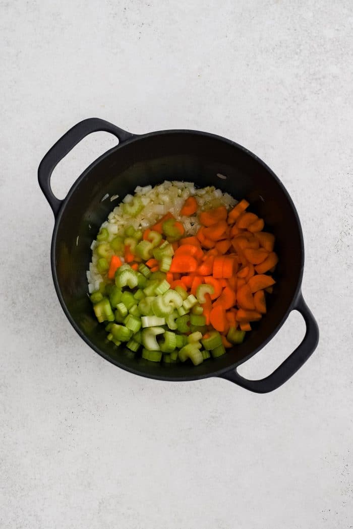 Chopped celery and carrots added to a large cast iron pot filled with softened onions in butter and olive oil.