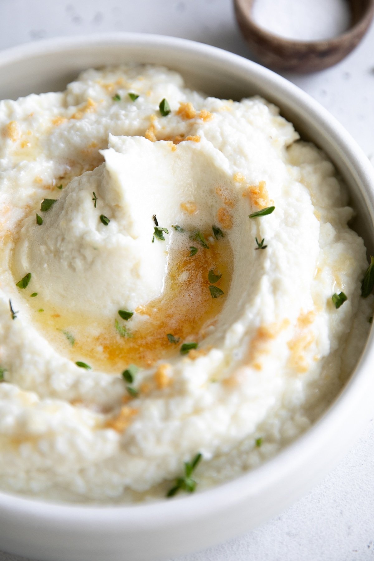 White serving bowl filled with creamy mashed cauliflower drizzled with brown butter and garlic.