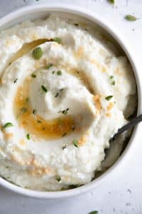 White serving bowl filled with creamy mashed cauliflower drizzled with brown butter and garlic.