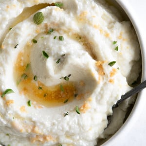White serving bowl filled with creamy mashed cauliflower drizzled with brown butter and garlic.