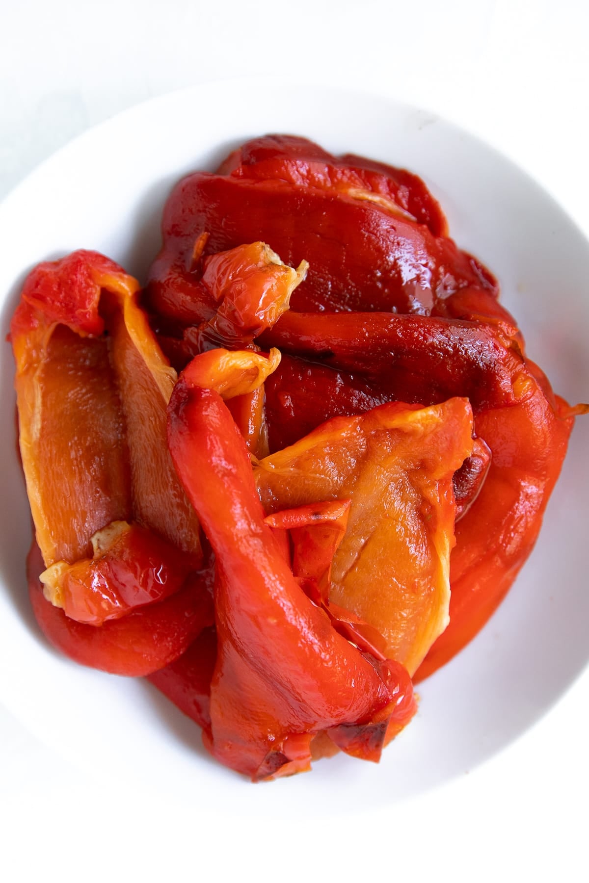 White bowl filled with roasted peeled red bell peppers.