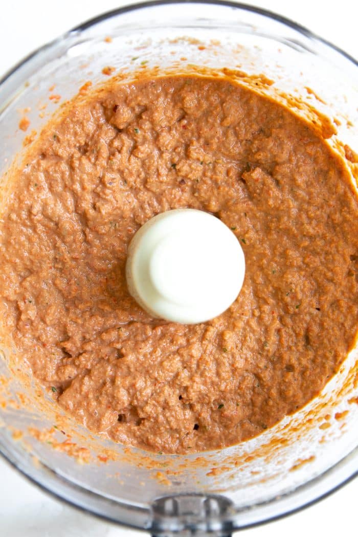 Large food processor filled with blended roasted red pepper and walnut dip.