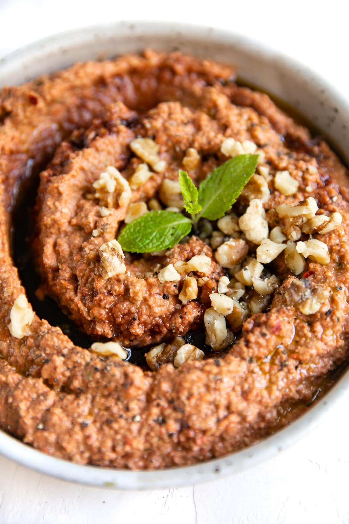 Muhammara dip in a large shallow bowl garnished with pomegranate molasses, chopped walnuts, and fresh mint.