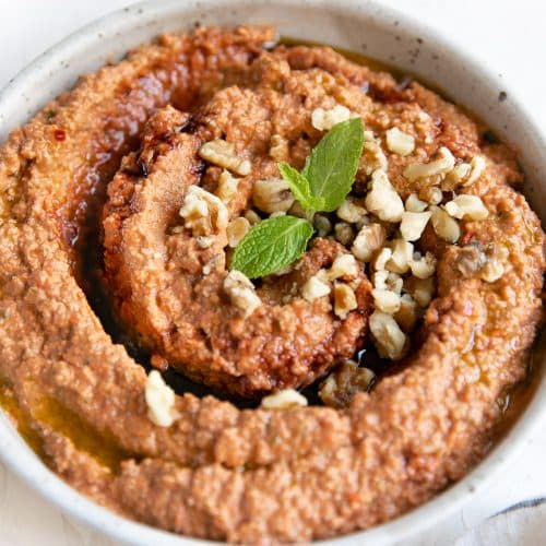 Muhammara dip in a large shallow bowl garnished with pomegranate molasses, chopped walnuts, and fresh mint.