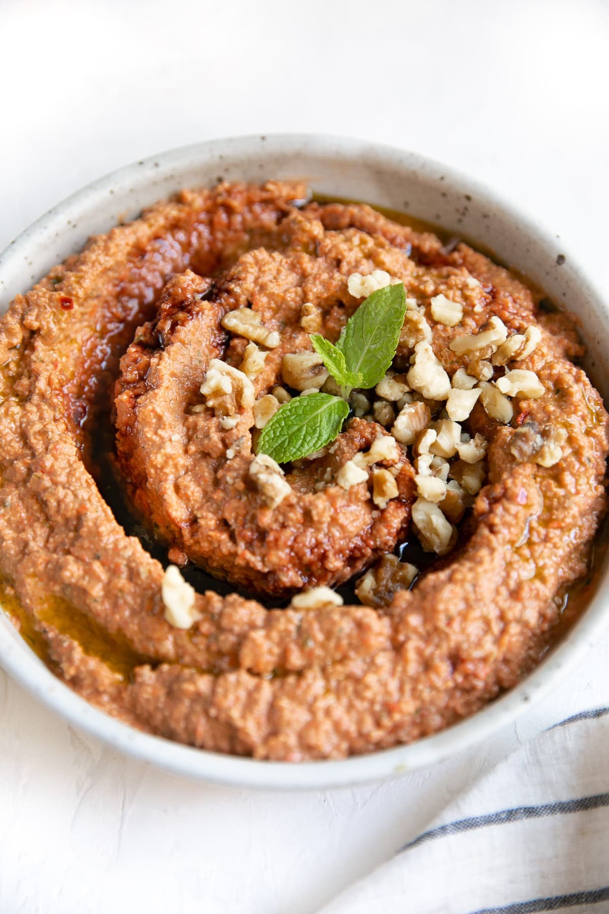 Muhammara dip in a large shallow bowl garnished with pomegranate molasses, chopped walnuts, and fresh mint.