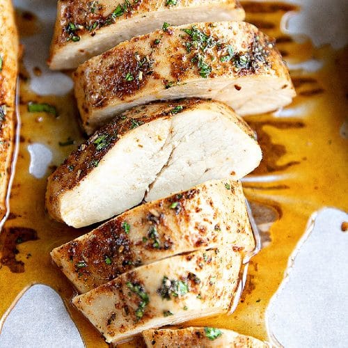 Golden juicy baked chicken breast sliced horizontally into thick strips and resting in its own juices.