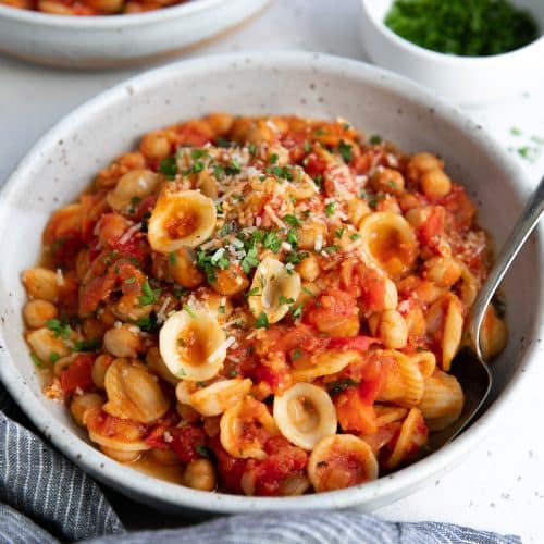 Pasta e Ceci made with tomatoes, pancetta, orecchiette pasta, and chickpeas, garnished with grated parmesan cheese and fresh parsley.