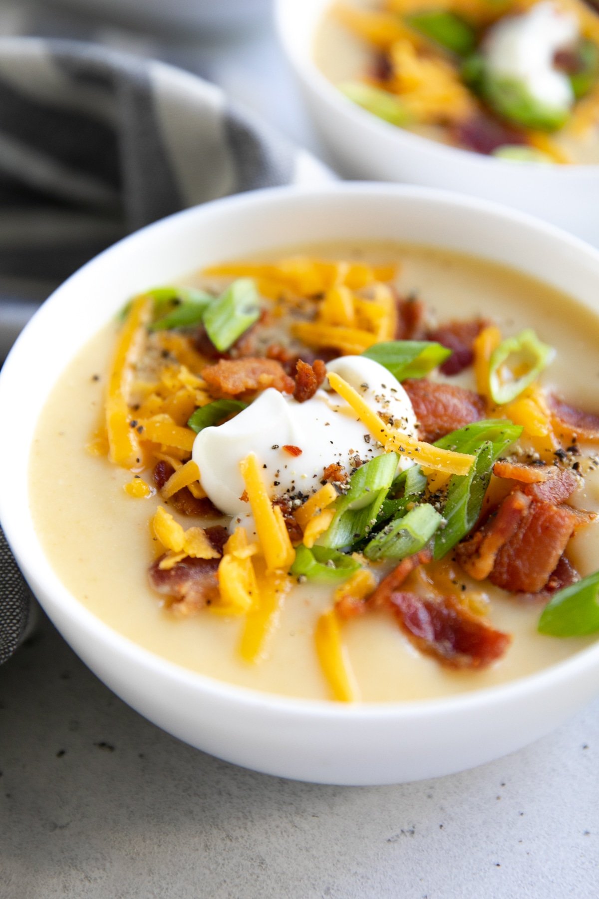White bowl filled with creamy potato soup and topped with green onions, sour cream, cheddar cheese, and bacon.