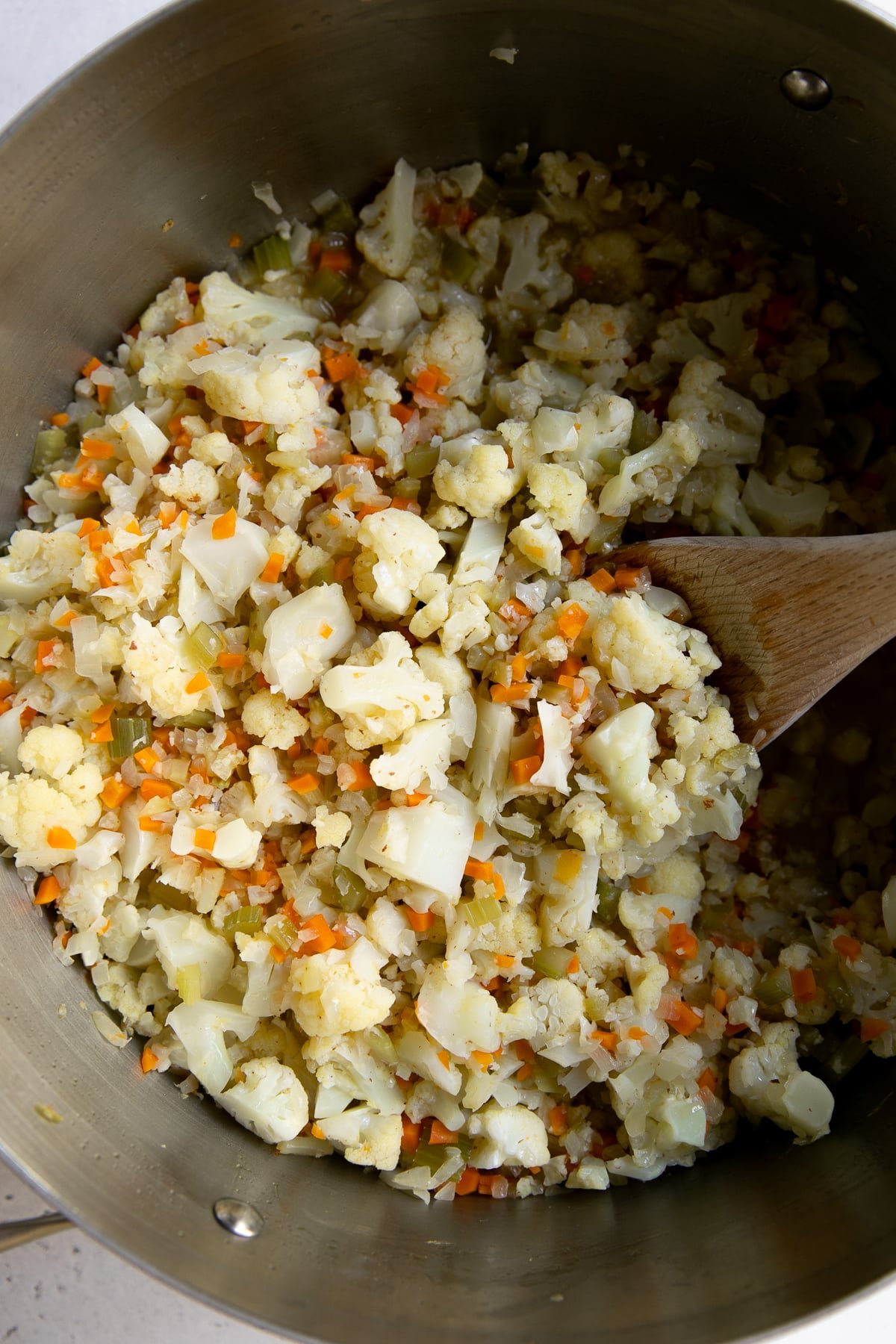 Finely minced onion, celery, and carrots, cooking in a large pot with finely chopped cauliflower.
